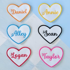 May include: Six heart-shaped embroidered patches with names: Daniel, Annie, Alley, Sean, Logan, and Taylor. Each patch has a white center with a different colored border and name in a matching color.