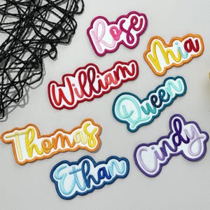 May include: A collection of embroidered name patches in a range of colours. Names such as "Rose", "William", "Mia", "Queen", "Thomas", "Ethan", and "Cindy" are displayed. Each patch has a white border.