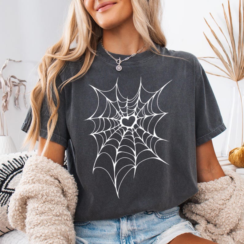 May include: Dark gray t-shirt featuring a white spiderweb design with a heart in the center. The shirt is a relaxed fit, perfect for casual wear. The design is centered on the front of the shirt.