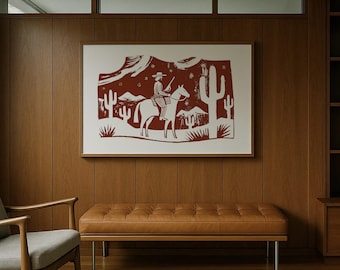 May include: A framed print depicting a cowboy on horseback in a desert scene. The artwork uses red and white tones, with cacti and mountains. The print is mounted above a brown leather bench.