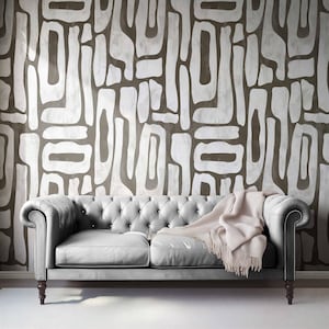 May include: A tufted, light gray leather sofa with rolled arms and dark wooden legs. A light pink throw blanket is draped over the sofa. The background features a brown and white abstract pattern.