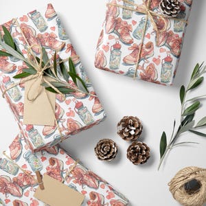 May include: Gift-wrapped presents with a white background. The wrapping paper features a watercolor pattern of running shoes, water bottles, and hearts in shades of pink and red. The gifts are tied with twine and decorated with pinecones and greenery.
