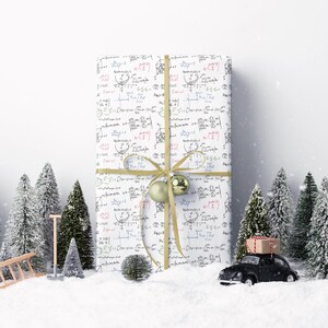 May include: A wrapped gift with a white background covered in mathematical equations, tied with a gold ribbon and bow. Two gold ornaments are attached to the bow. The gift is surrounded by miniature Christmas trees, snow, and a toy car.