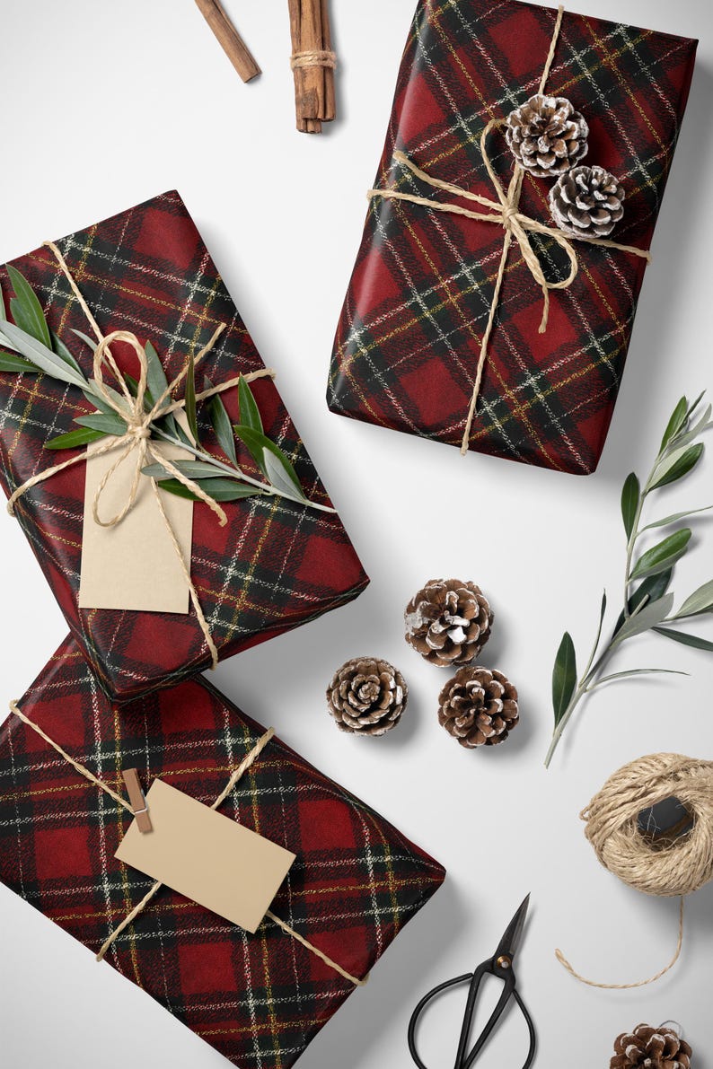 May include: Overhead shot of wrapped gifts with red plaid paper, tied with twine and adorned with sprigs of greenery and pinecones. A pair of scissors and a spool of twine are also present, suggesting a holiday or special occasion theme.