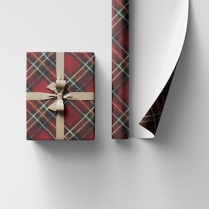 May include: A wrapped gift box and a roll of wrapping paper, both featuring a red, black, and gold plaid pattern. The gift is tied with a tan ribbon. The paper is partially unrolled, revealing a white interior.