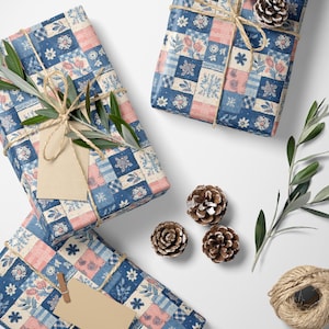 Puede incluir: Regalos envueltos en papel de retazos florales azules, rosas y blancos, atados con hilo y adornados con piñas y ramas de olivo. Una etiqueta en blanco está adjunta a un regalo. También se ven tijeras y un ovillo de hilo.