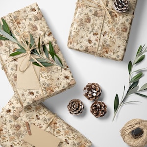 May include: Several wrapped gifts with a bee and floral pattern, tied with twine and adorned with sprigs of greenery and pinecones. A blank tag is attached to one gift. Scissors and a spool of twine are also present.