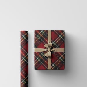 May include: A wrapped gift box and a roll of wrapping paper. Both are covered in a red, black, and gold plaid pattern. The gift box is tied with a tan ribbon and bow, creating a festive presentation.