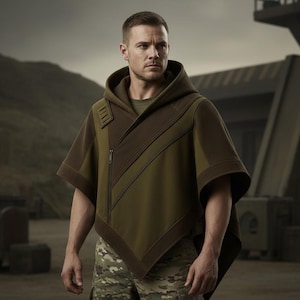 May include: An olive green hooded poncho with a brown accent panel and a diagonal zipper. The poncho has a relaxed fit and is worn over a green shirt and camouflage pants. The background features a mountainous landscape and industrial structures.