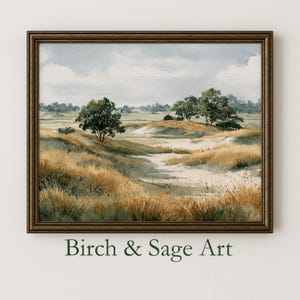Puede incluir: Una pintura de paisaje en acuarela enmarcada que presenta un campo sereno con hierbas altas y doradas y árboles dispersos bajo un cielo nublado. La obra de arte está en un marco marrón oscuro, con el texto "Birch & Sage Art" en la parte inferior.