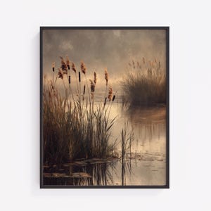 May include: A framed landscape print depicts a serene waterscape. Tall reeds and grasses in shades of brown and green line the water's edge. The water reflects the sky, creating a soft, muted color palette. The artwork is framed in a black border.