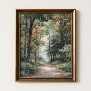 May include: A rectangular wall art print featuring a forest path scene enclosed in a dark metallic gold frame. The painting depicts tall trees with green and autumn-toned foliage lining a dirt trail that leads into a bright, hazy background.