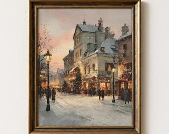 May include: A framed painting depicting a snowy European town square at dusk. The scene features multi-story buildings with snow-covered roofs, glowing street lamps, and people walking along a snow-dusted street under a soft pink and orange sky.