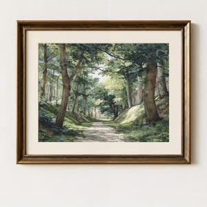 以下が含まれることがあります： 金色の木製フレームに入った、森の小道の水彩画。このアートワークは、緑豊かな木々や葉の間を縫うように進む日当たりの良い小道を描いており、穏やかな風景シーンを作り出しています。