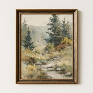 May include: A framed landscape painting depicting a misty forest scene with tall evergreen trees, a flowing stream, and scattered rocks. The color palette features muted greens, earthy browns, and soft grays, all enclosed within a dark metallic frame.