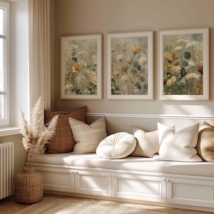 Può includere: Tre stampe artistiche floreali incorniciate con fiori beige e gialli sono appese sopra una panca bianca con cuscini. La stanza ha una palette di colori neutri con un vaso intrecciato ed erba della pampa nell'angolo.