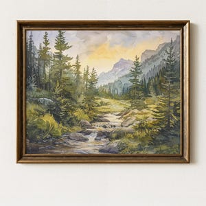 May include: A framed watercolour painting depicting a mountain landscape. The artwork shows a stream winding through a valley, with evergreen trees and mountains in the background. The sky transitions from yellow to blue. The frame is golden-brown.