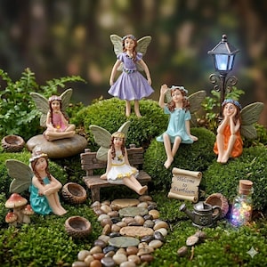 May include: A miniature fairy garden scene featuring six fairy figurines with wings, dressed in various pastel-colored dresses. The scene includes a miniature bench, a street lamp, and a sign that reads "Welcome to Everbloom."