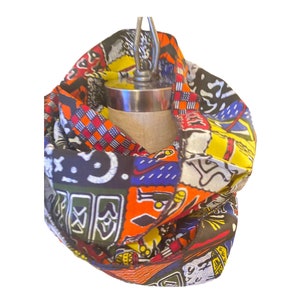 May include: A colorful infinity scarf with a patchwork design featuring geometric patterns, abstract shapes, and stylized figures. The scarf is made of fabric with a textured surface and is folded into a loop.