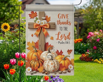 May include: A garden flag featuring a wooden cross with an orange bow, surrounded by fall leaves and pumpkins. The flag reads "GIVE thanks TO THE Lord - Psalm 136:1". The design is set against a beige background, perfect for autumn decor.