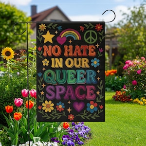 以下が含まれることがあります： レトロなスタイルのカラフルな文字で「NO HATE IN OUR QUEER SPACE」と書かれた黒いガーデンフラッグ。旗には虹、星、平和のシンボル、花のアクセントが描かれています。庭の装飾品です。