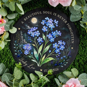 May include: Round black slate memorial stone with a painted floral design. The artwork features blue forget-me-nots, a full moon, and the text "A BEAUTIFUL SOUL IS NEVER FORGOTTEN." Includes the name "Baby Leo" and the date 03.06.2026.