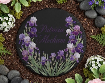 May include: A round, black slate garden stone featuring a watercolor design of purple and white irises. The name "Patricia Mecham" is written in a matching purple script across the center of the stone. The stone is surrounded by flowers and greenery.