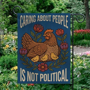 May include: A blue garden flag with the text "CARING ABOUT PEOPLE IS NOT POLITICAL". The flag features a brown hen with three yellow chicks, surrounded by red and purple flowers. The flag is hanging in a garden.