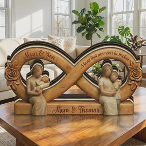 May include: Wooden infinity sculpture with carved figures of a mother and child. The sculpture has the text "Mom & Son" and "A bond that can never be broken". The base reads "Mom & Thomas". The sculpture is brown with black and white accents.