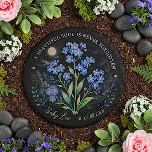 May include: A round black stone garden memorial with a floral design. The memorial features blue forget-me-nots, the text "A BEAUTIFUL SOUL IS NEVER FORGOTTEN", and the name "Baby Leo" with a date.