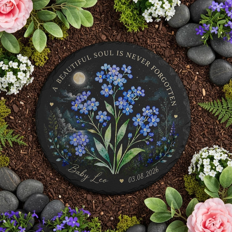 May include: A round black stone garden memorial with a floral design. The memorial features blue forget-me-nots, the text "A BEAUTIFUL SOUL IS NEVER FORGOTTEN", and the name "Baby Leo" with a date.