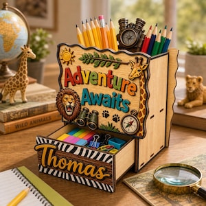 May include: A wooden desk organiser with the words "Adventure Awaits" and a drawer labelled "Thomas". The organiser features a lion, giraffe, compass, and binoculars. Pencils and a small compass are inside.