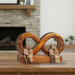 Peut inclure: Sculpture en bois en forme de symbole infini avec deux couples, l'un jeune et l'autre âgé, assis sur une base. La sculpture porte les inscriptions "From our first kiss" et "Till our last breath". La base est gravée de "James & Sophia".