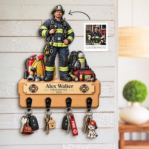 May include: A wooden wall-mounted key holder featuring a 3D firefighter figure, firefighting equipment, and a custom photo insert. A brass-coloured plaque displays the text Alex Walter FIREFIGHTER 2026. Four black metal hooks hold various keychains.