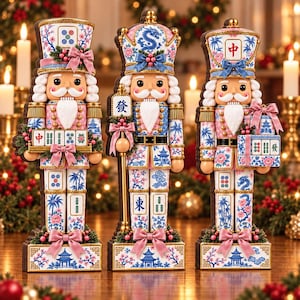 May include: Three nutcracker figures decorated with blue and pink floral patterns and mahjong tile motifs. Each figure features a white beard, a tall hat, and pink bows. The figures display various Chinese characters and blue pagoda illustrations.
