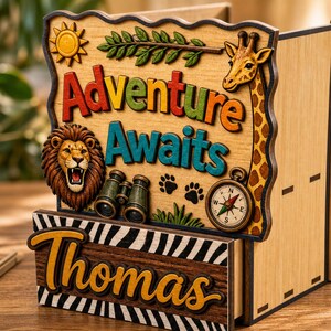 May include: Wooden desk organiser with a safari theme. Features the words "Adventure Awaits" in colourful letters, a lion, giraffe, compass, binoculars, and paw prints. The name "Thomas" is also displayed.