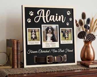 May include: A personalized pet memorial frame with three photos of a dog, paw prints, and the name "Alain." The frame includes the text "Puppy Days," "Our Alain 2018-2026," and "Joyful Heart." A brown leather collar is attached.