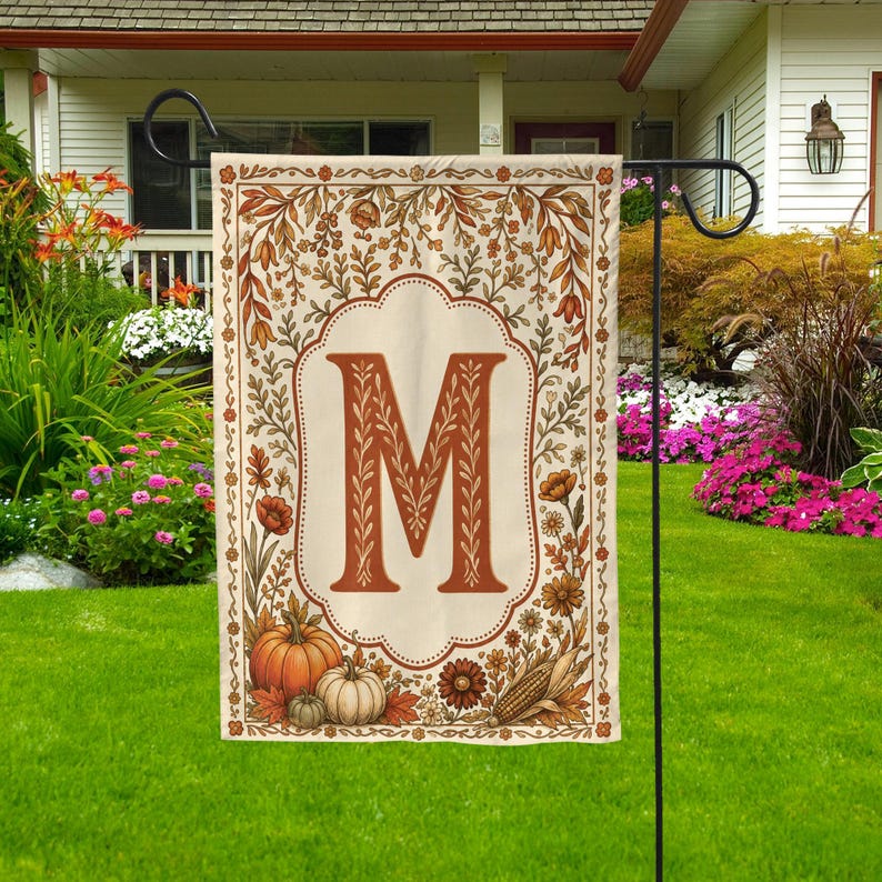 May include: A rectangular garden flag featuring a large, centered letter M in a serif font. The design is framed by a border of autumn-themed illustrations, including orange pumpkins, white gourds, corn, and various fall flowers and foliage.