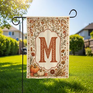 May include: A rectangular garden flag featuring a cream-colored center with a large, ornate orange letter M. The border is decorated with autumn-themed illustrations including orange pumpkins, brown corn, and various fall-colored leaves and flowers.