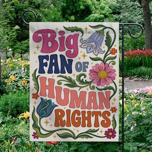 Może przedstawiać: Flaga ogrodowa z napisem "Big Fan of Human Rights" w stylu retro. Flaga zawiera kwiatowe i gwiazdowe wzory w kolorach różowym, niebieskim, pomarańczowym i zielonym na kremowym tle. Flaga jest eksponowana na czarnym metalowym paliku ogrodowym.
