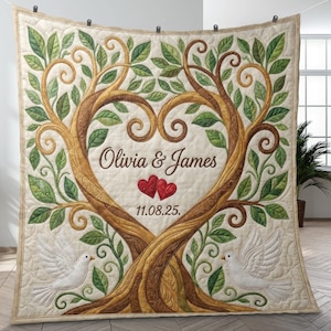 May include: A beige quilted blanket featuring a tree design with a heart-shaped center. The tree has brown branches, green leaves, and the names "Olivia & James" with the date "11.08.25". Two white doves are at the bottom.