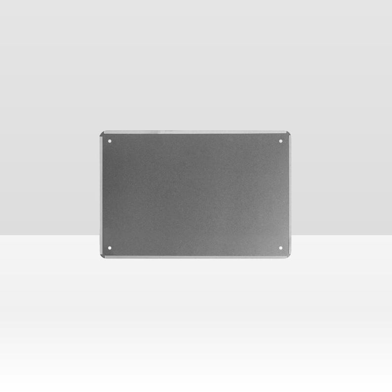 May include: A rectangular, gray metal sign with rounded corners and four visible mounting holes. The sign has a smooth, matte finish and is set against a plain, light background. The sign is a simple, minimalist design.