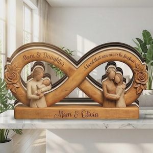 Puede incluir: Escultura de madera con forma de signo de infinito con figuras talladas de una madre y un niño, y una madre y una hija. La escultura tiene las inscripciones "Mom & Daughter", "A bond that can never be broken" y "Mom & Olivia". Con tallas de rosas.
