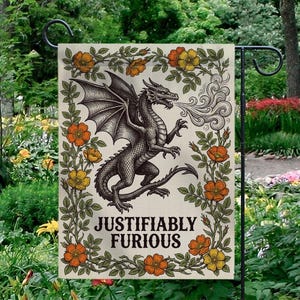 May include: A garden flag featuring a detailed illustration of a dragon exhaling smoke, with the text "JUSTIFIABLY FURIOUS" below. The dragon is surrounded by a floral border of orange and yellow flowers and green leaves. The flag is displayed outdoors.