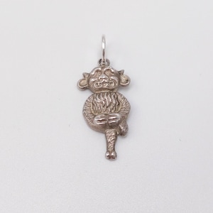 May include: A silver pendant depicting a stylized animal figure, possibly a monkey or lion. The pendant has a loop for a chain and features textured fur and facial details. The pendant is set against a white backdrop.