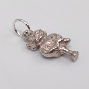 May include: A silver poodle charm. The charm is detailed with the poodle's fur, legs, and tail. It has a small loop at the top for attaching to a necklace or bracelet. The charm is on a white background. The charm is made of silver.