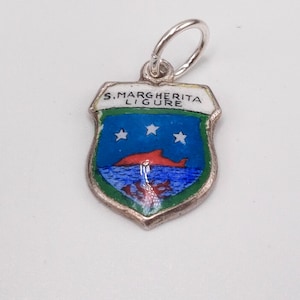 May include: A silver charm with a shield design. The shield features a blue background with three white stars, a red dolphin, and the text "S. MARGHERITA LIGURE". The charm has a silver loop at the top.