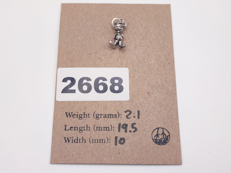 Pode incluir: Um berloque de metal prateado em forma de personagem de rato de desenho animado. O berloque &eacute; exibido num cart&atilde;o castanho com o n&uacute;mero 2668, um peso de 2,1 gramas, um comprimento de 19,5 mm e uma largura de 10 mm, com uma argola.