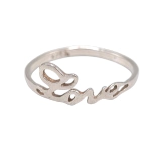 May include: A silver ring with the word "Love" in a cursive font. The ring is made of a shiny, light-colored metal and is set against a white background. The ring is a delicate piece of jewelry.