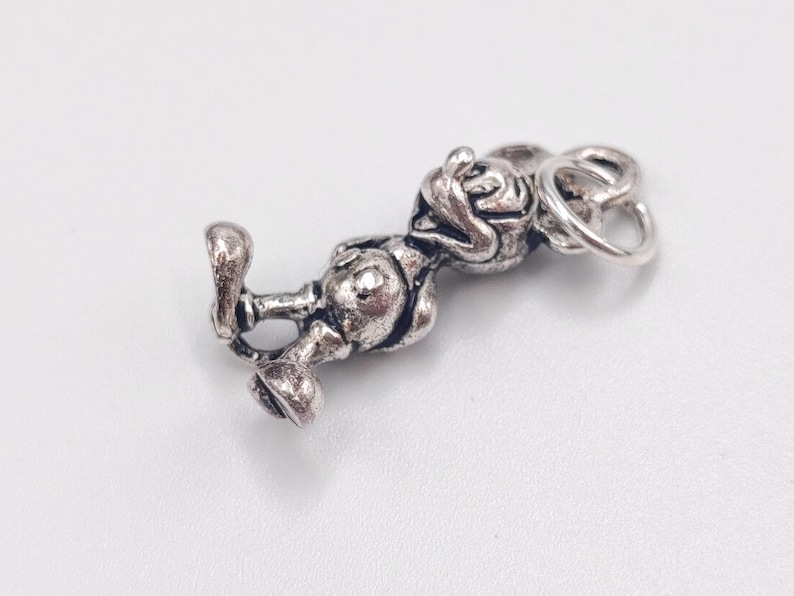 Pode incluir: Um berloque de metal em tom prateado apresentando uma figura tridimensional de um rato de desenho animado com orelhas grandes, vestindo shorts e sapatos, com um pequeno anel circular preso ao topo da cabe&ccedil;a para pendurar.